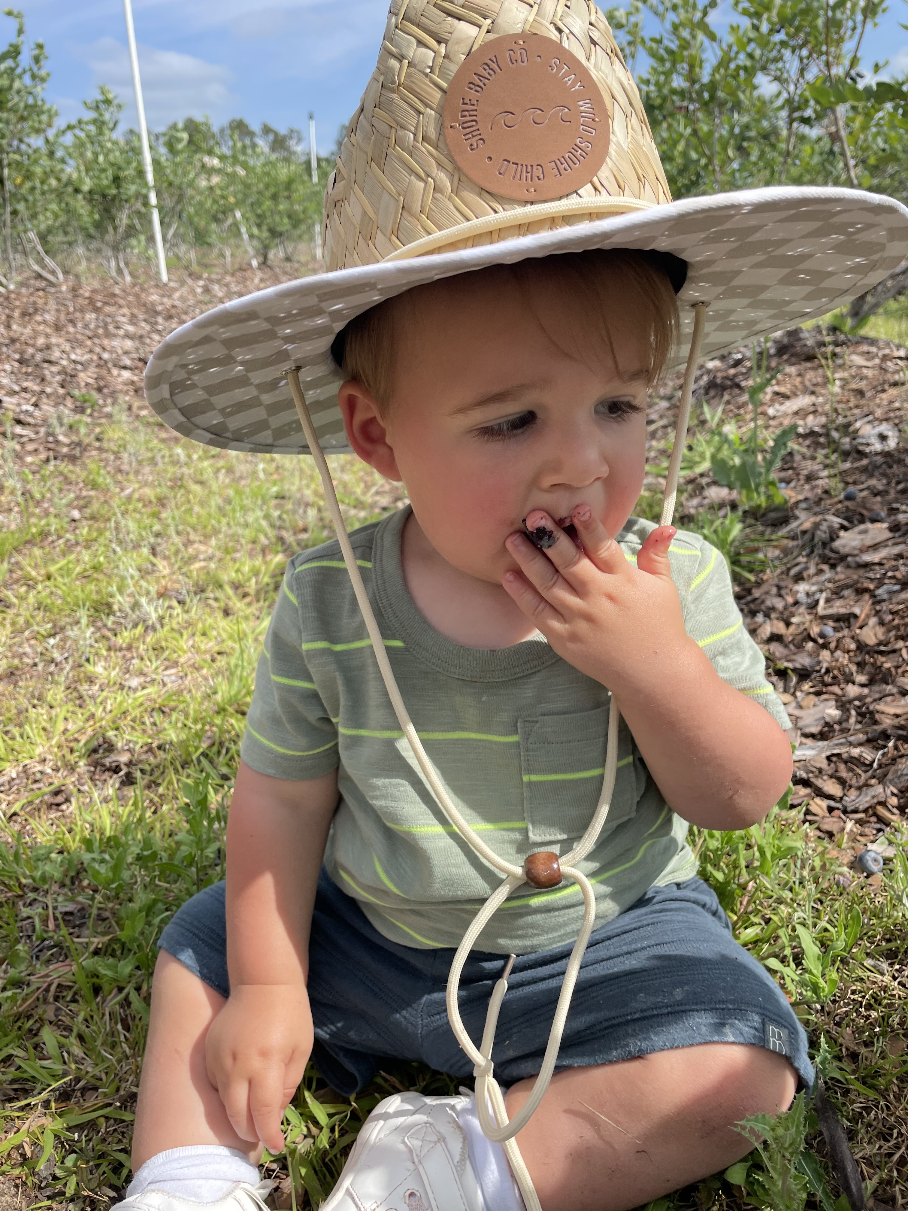 Toddler in straw hat eating blueberries